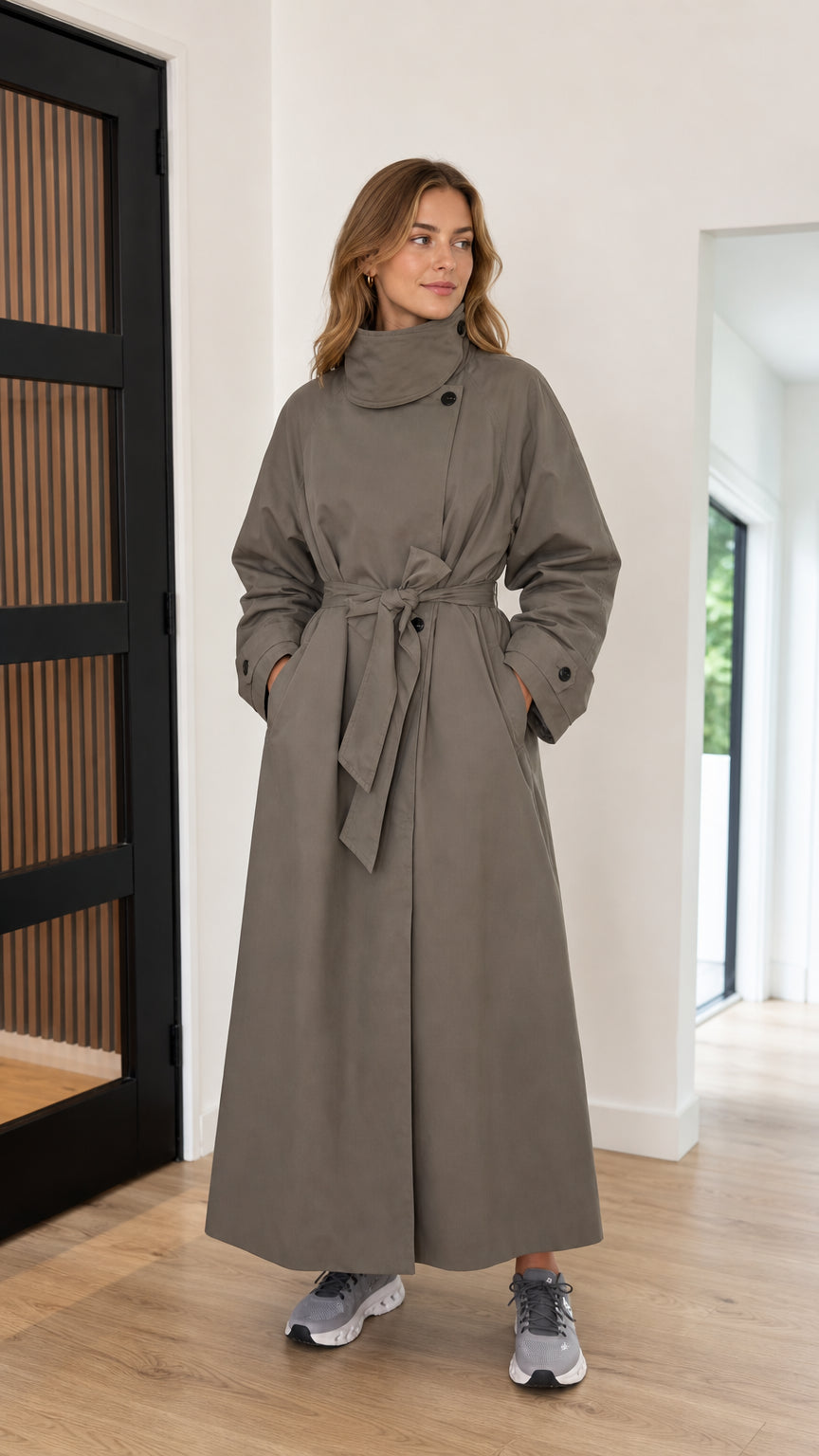 Front full-length view of woman wearing taupe high neck maxi trench coat with tie belt