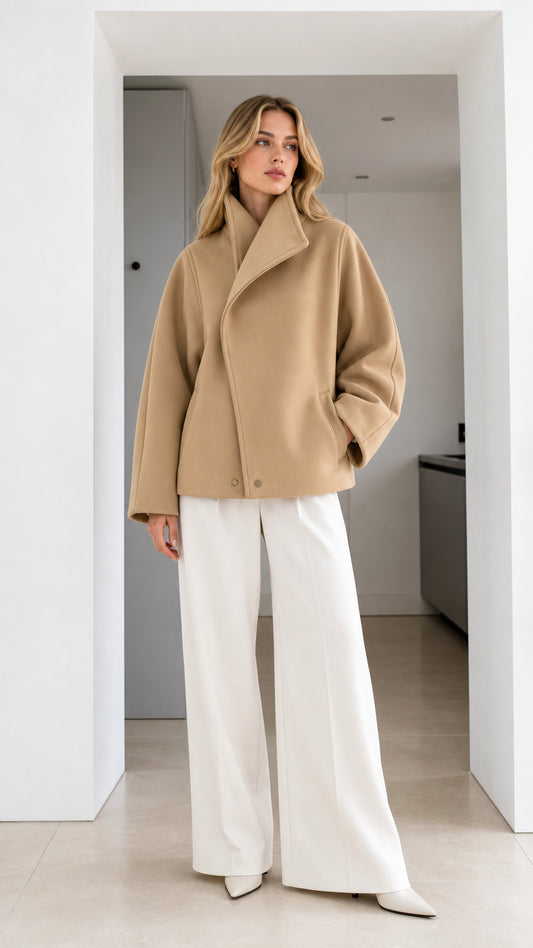 Front full-length view of model wearing camel asymmetrical high-neck jacket with white wide-leg trousers