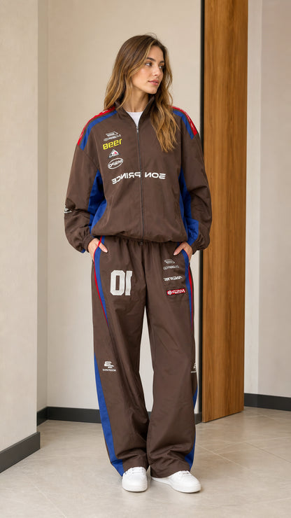 Front full view of woman wearing brown retro racing graphic two-piece tracksuit set with blue and red accents