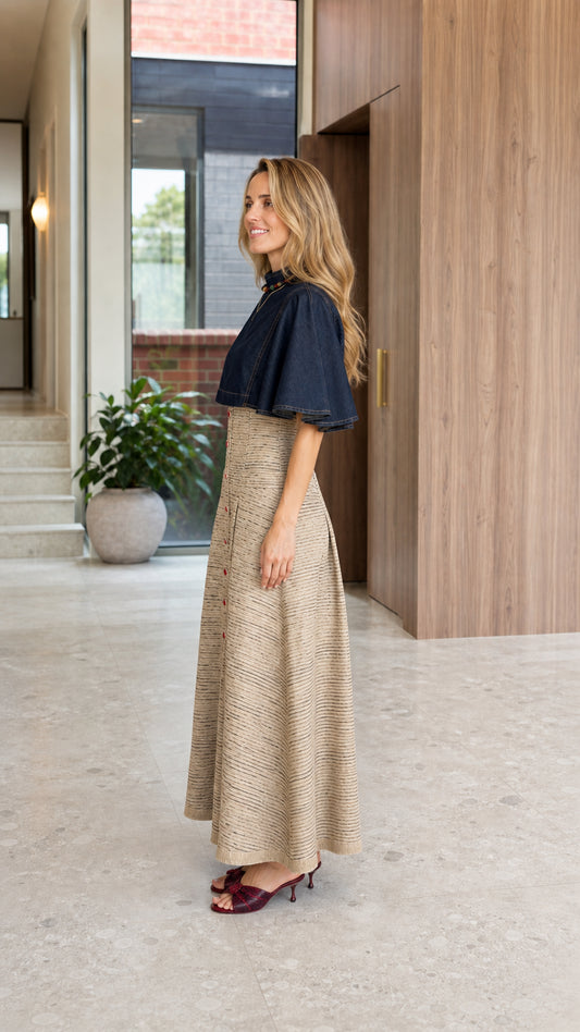 Side angle view of woman modeling the capelet high-waist pleated maxi dress in Navy Blue