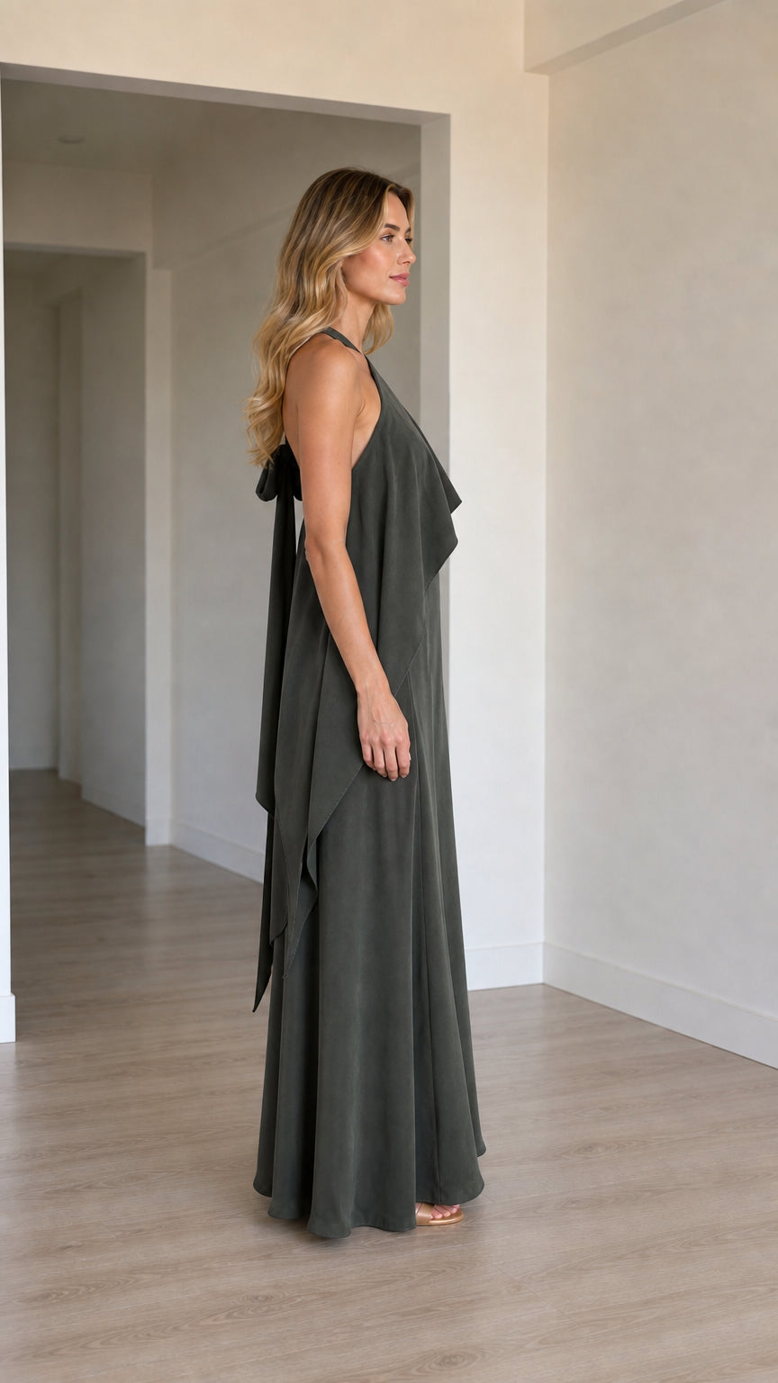 Side profile of a model wearing a charcoal one-shoulder evening gown with layered drape