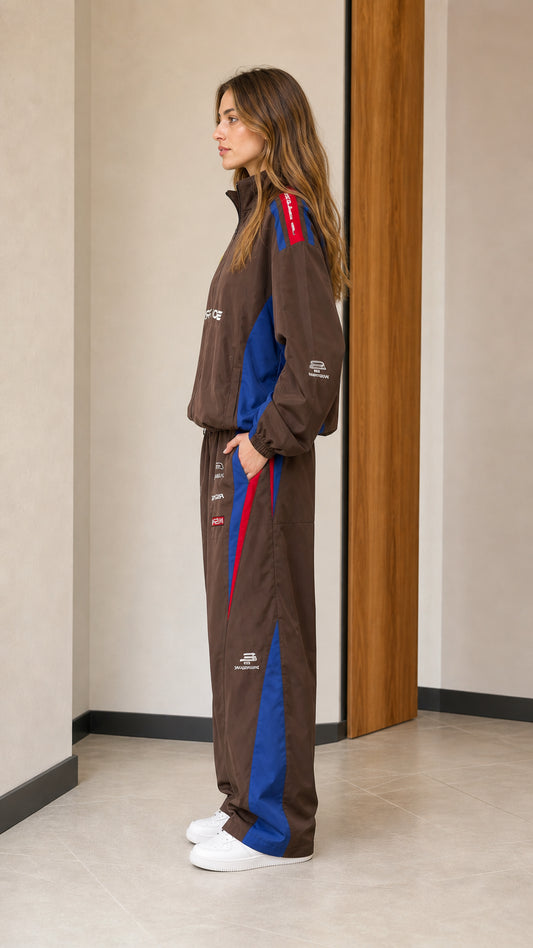 Side profile of woman wearing brown graphic windbreaker jacket and wide-leg track pants