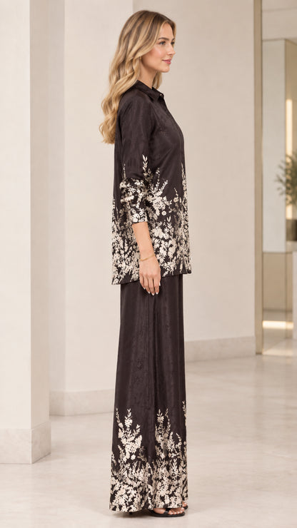 Side profile view of women's floral satin matching shirt and pant set in black