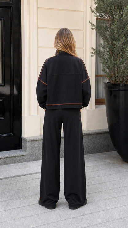 Back view of model showing contrast seam details on black zip jacket and wide-leg trousers