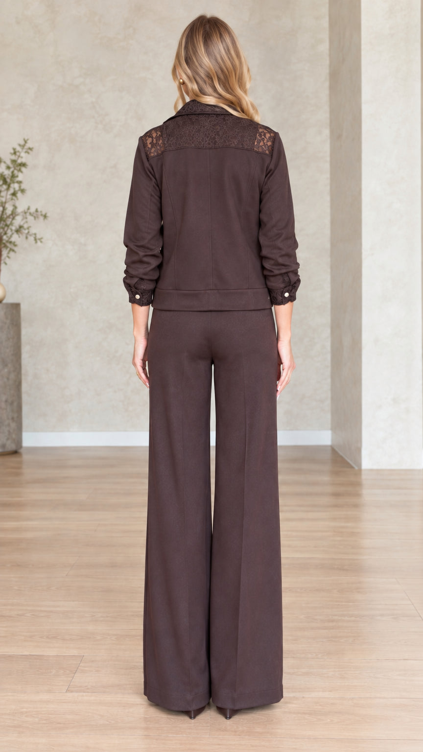 Back view of model showing lace yoke detail on dark brown jacket and straight wide trousers