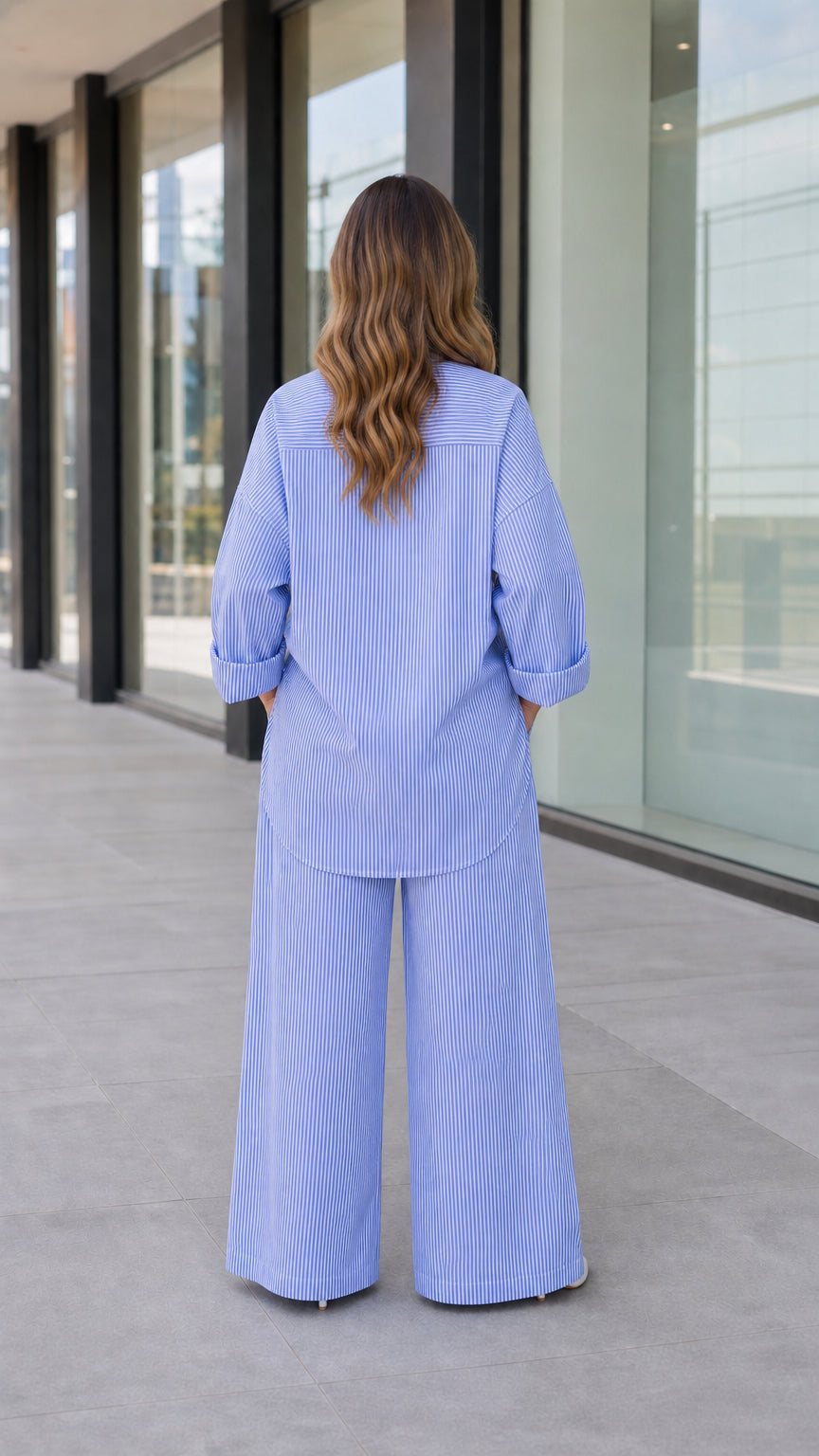 Back full-length view of woman wearing blue striped oversized shirt and wide-leg trousers
