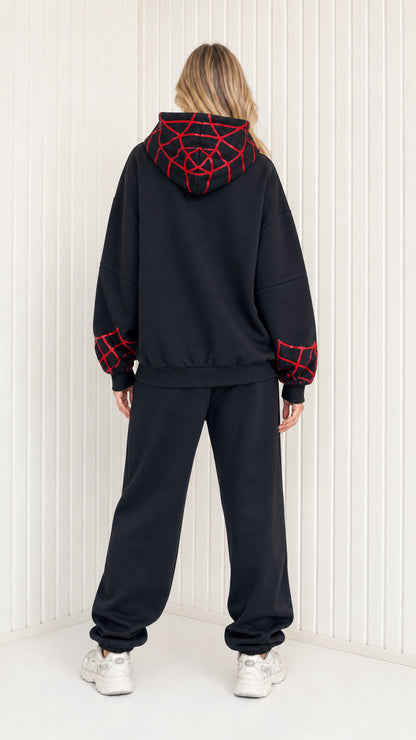 Back view of model showing graphic web details on hoodie of black sweatsuit set