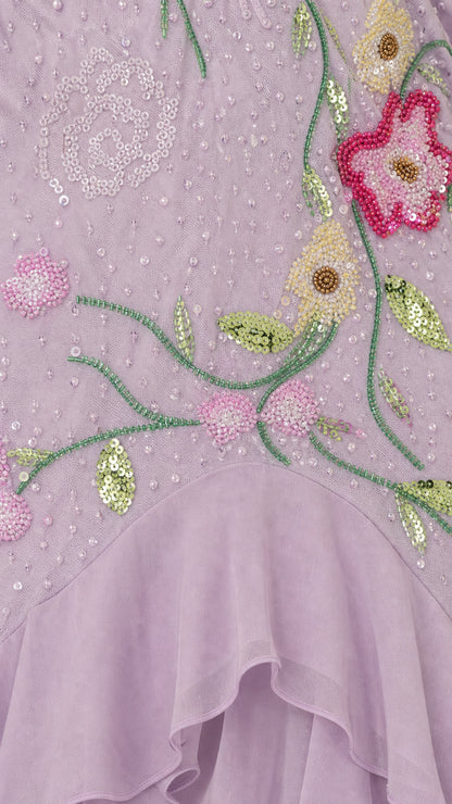 Close-up detail of floral beadwork, sequins, and layered chiffon ruffle hem on lavender dress