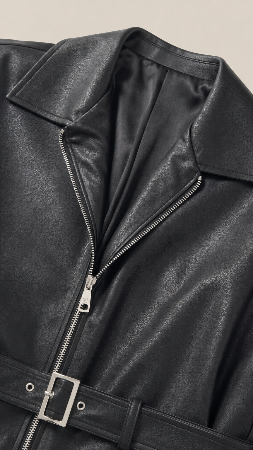 Close-up detail of black faux leather jacket front zipper, wide collar, and belted buckle hem