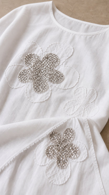 Close up view of white textured fabric with beaded floral embroidery and round neckline