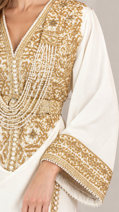 Close-up detail of ornate gold-tone embroidery and bead-like accents on white bodice