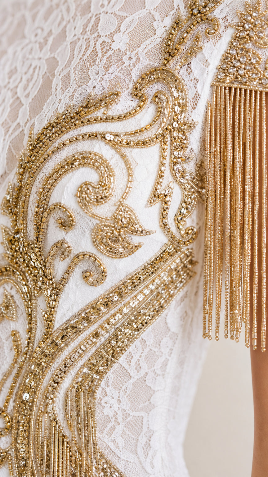 Close-up detail of textured lace fabric, gold sequins, metallic embroidery, and hanging beaded tassel sleeve