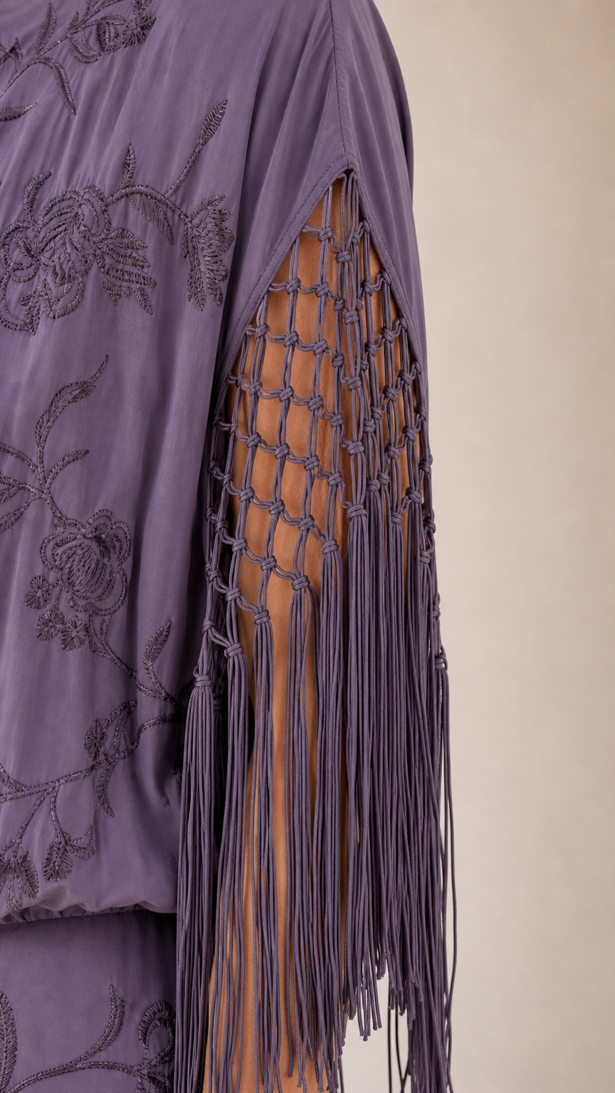 Close-up of macrame openwork fringe sleeve and embroidered fabric details