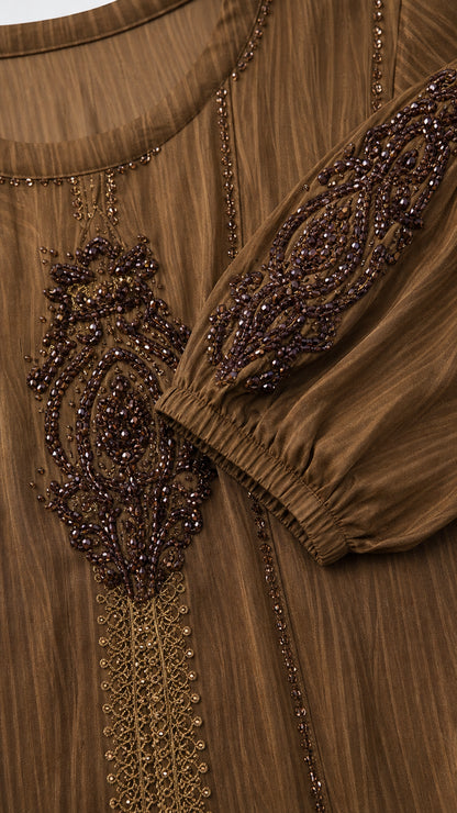 Close-up detail of ornate beadwork and embroidery on chest and cuffs of brown dress