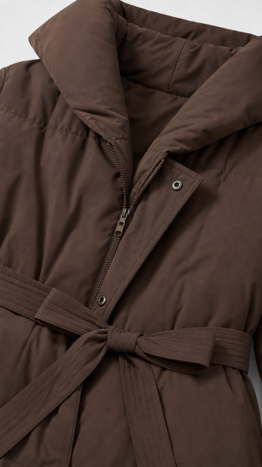 Close-up detail of zipper, snap button placket, and tie belt on chocolate brown puffer coat