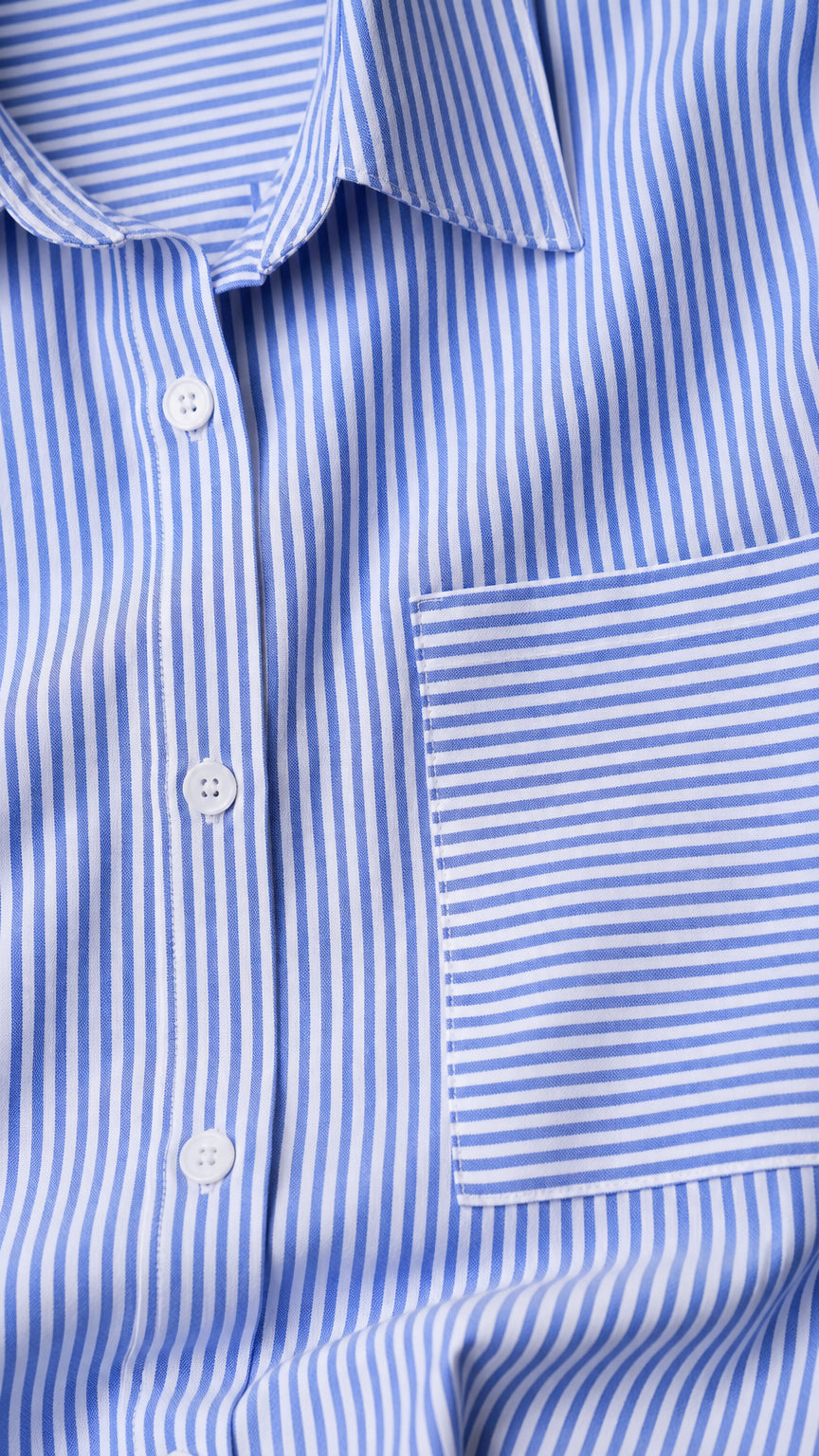 Close-up detail of blue vertical striped woven fabric, spread collar, buttons, and horizontal-striped chest pocket