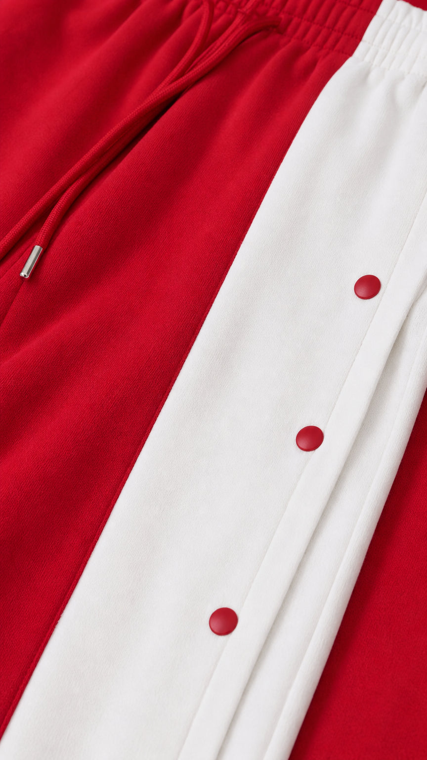 Close-up detail of red track pants showing drawstring waist and white side panel with red snap buttons