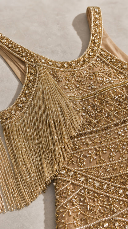 Close-up detail of neckline, intricate beadwork, and fringe trim on gold evening gown