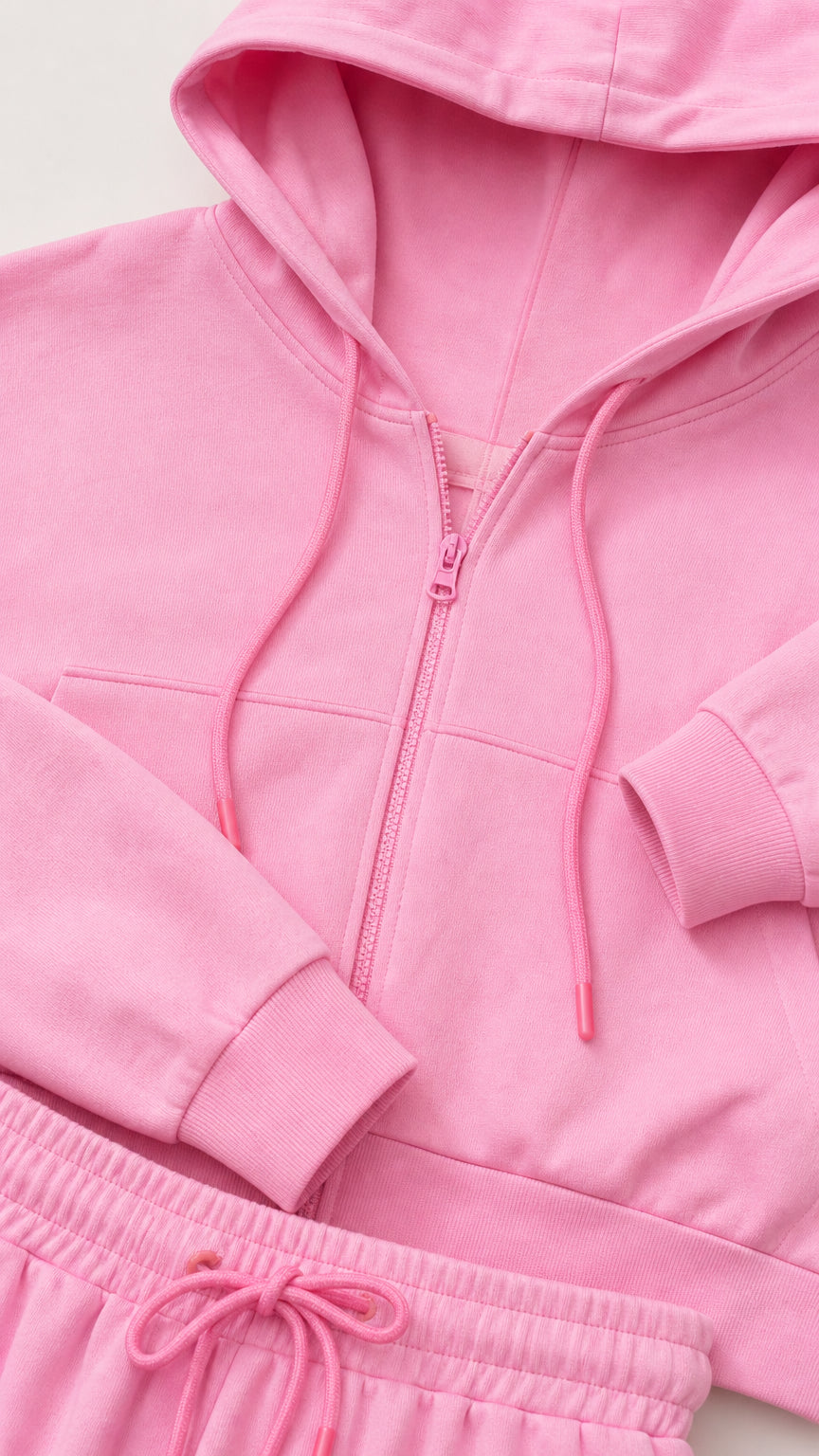 Close-up detail of pink cropped hoodie zipper, hood drawstrings, and waistband
