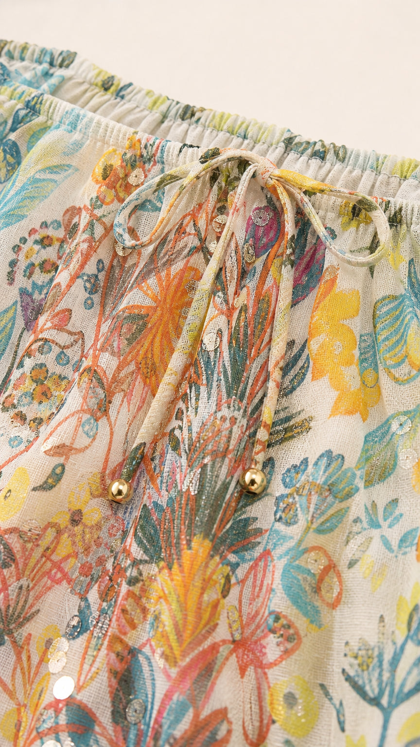Close-up detail of neckline drawstring with gold beads and lightweight floral fabric texture