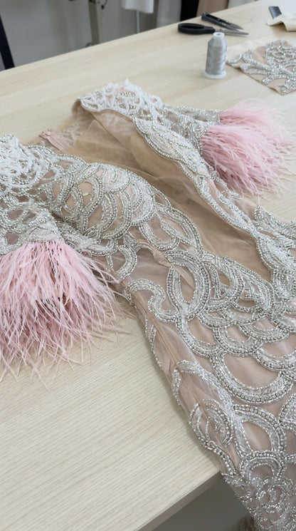 Close-up detail of silver embroidery, beadwork, and pink feather cuff