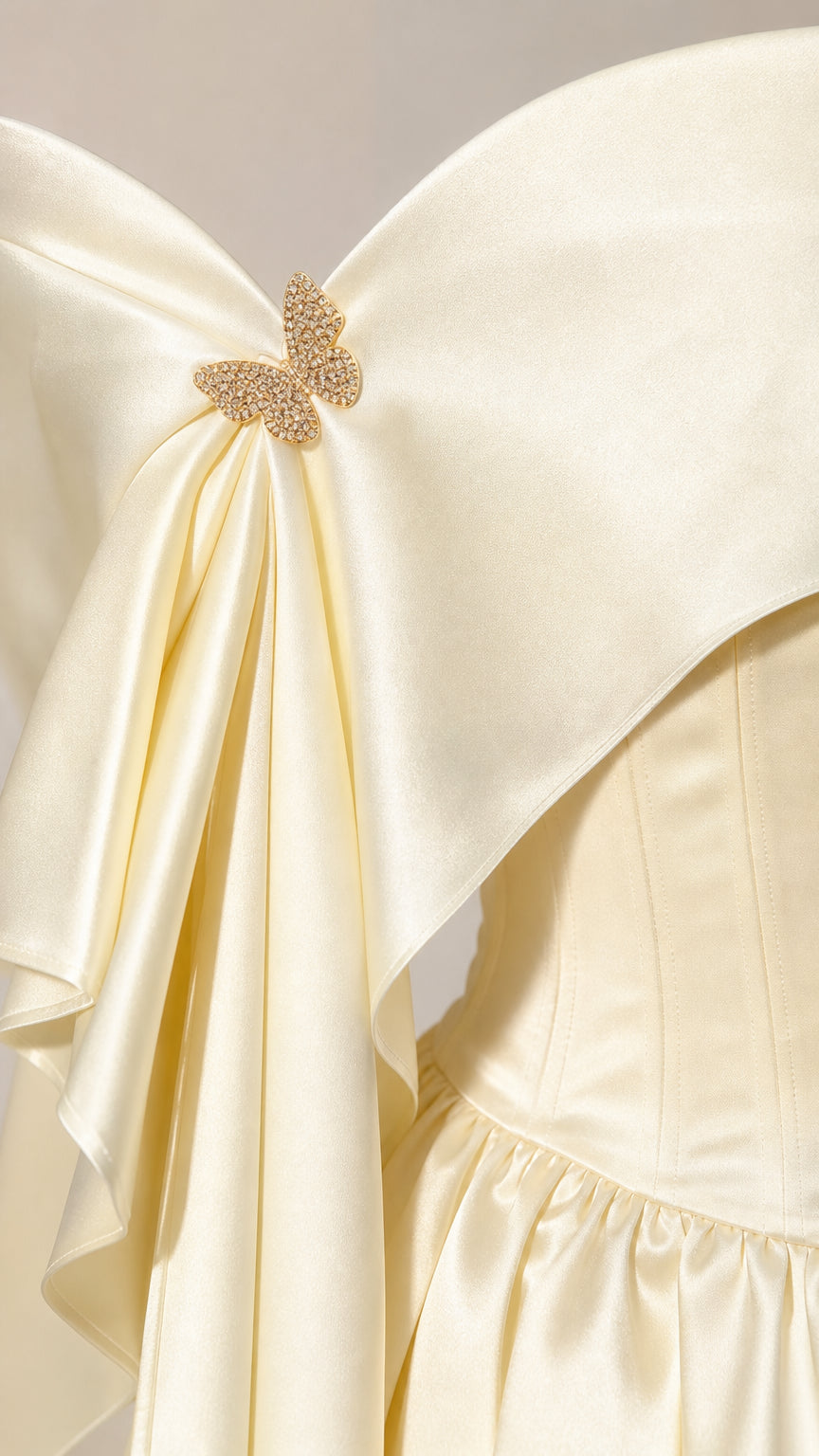 Close-up detail of off-the-shoulder neckline with satin fold and sparkling gold crystal butterfly brooch