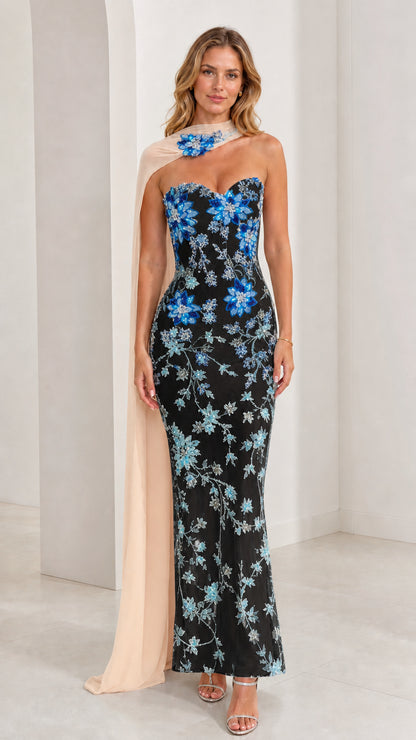 Model wearing black strapless evening gown with blue floral beadwork and chiffon cape