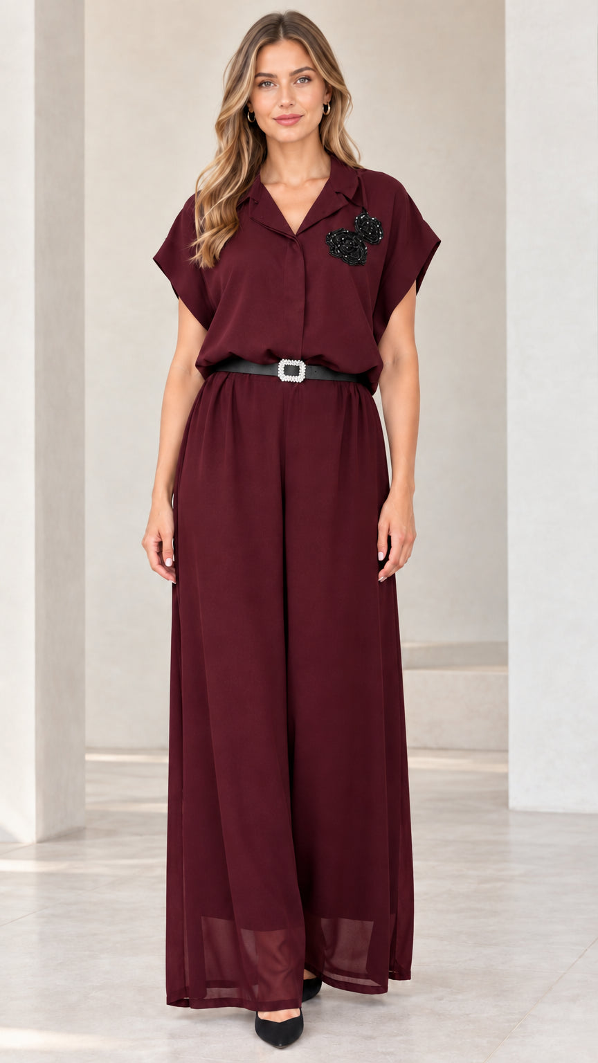 Front view of woman wearing burgundy wide-leg jumpsuit with floral appliqué