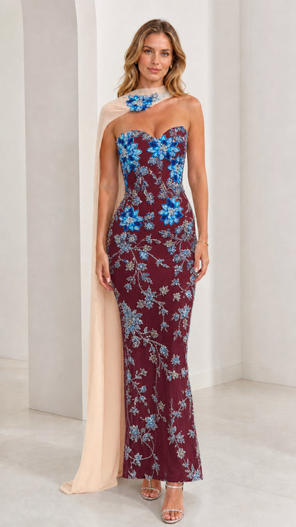 Model wearing burgundy strapless evening gown with blue floral beadwork and chiffon cape
