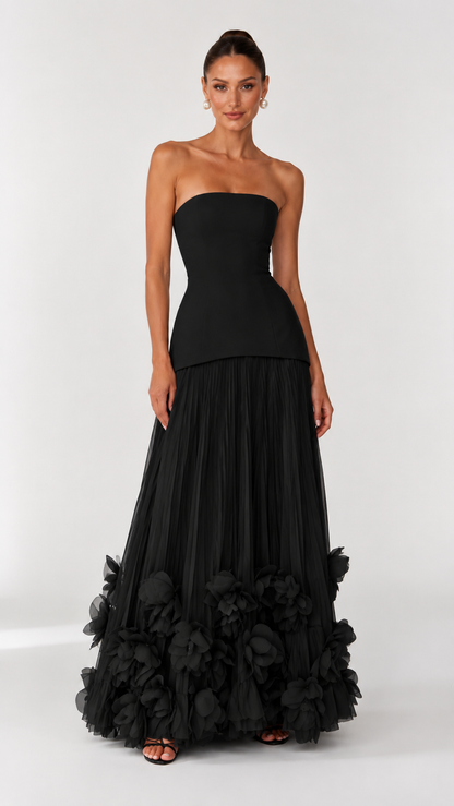 Front view of black strapless maxi dress with pleated skirt and dramatic floral hem